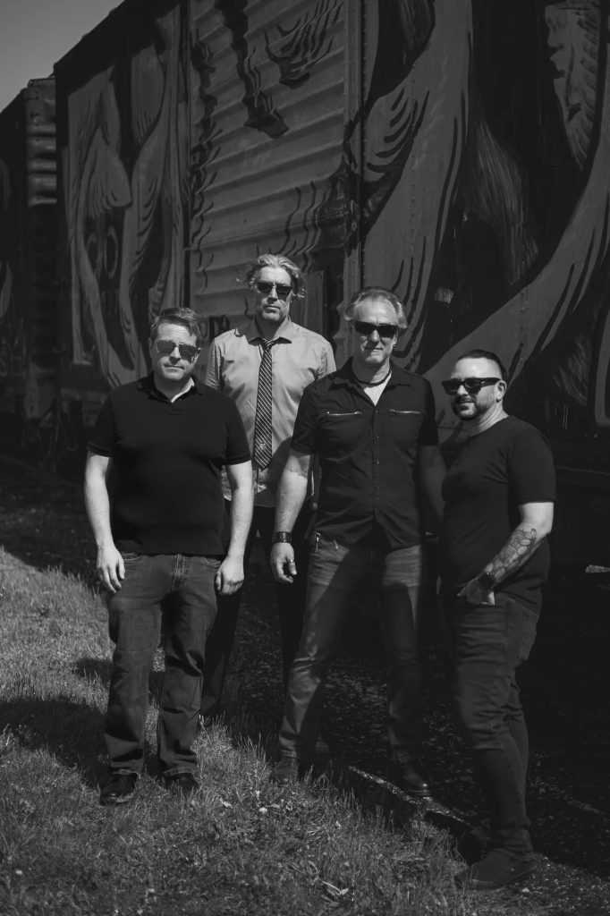 Boxcar Junction, four band members standing beside a mural-painted boxcar (black and white).