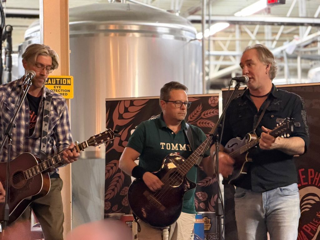 Three members of Boxcar Junction performing in front of brewery tanks at Railway City.